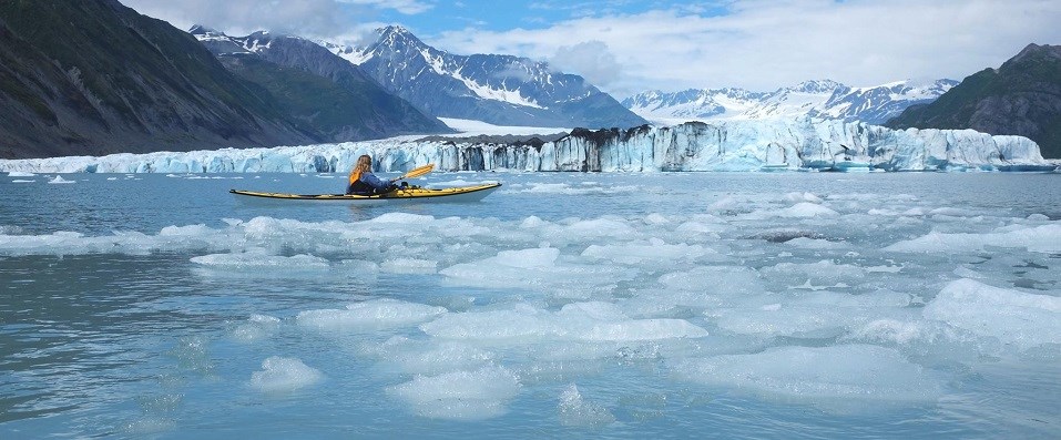 KayakingKEFJ A kayaker paddles through ice in front of a glacier.