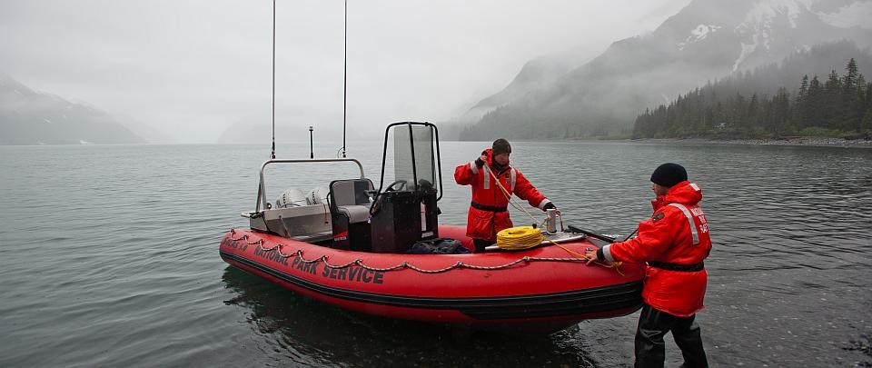 two park employees pull a boat on shore in a misty inlet