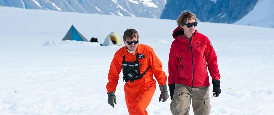 two men walk on an ice field with tents in the background two men walk on an ice field with tents in the background