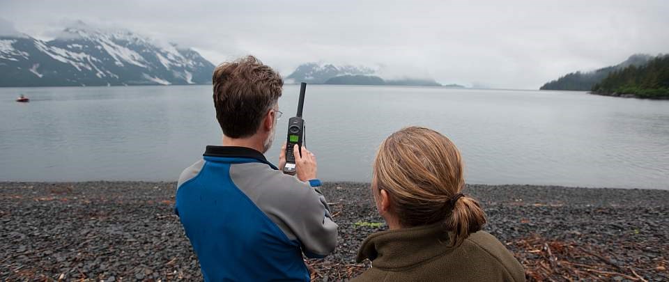a man uses a satellite phone next to a women on a foggy beach