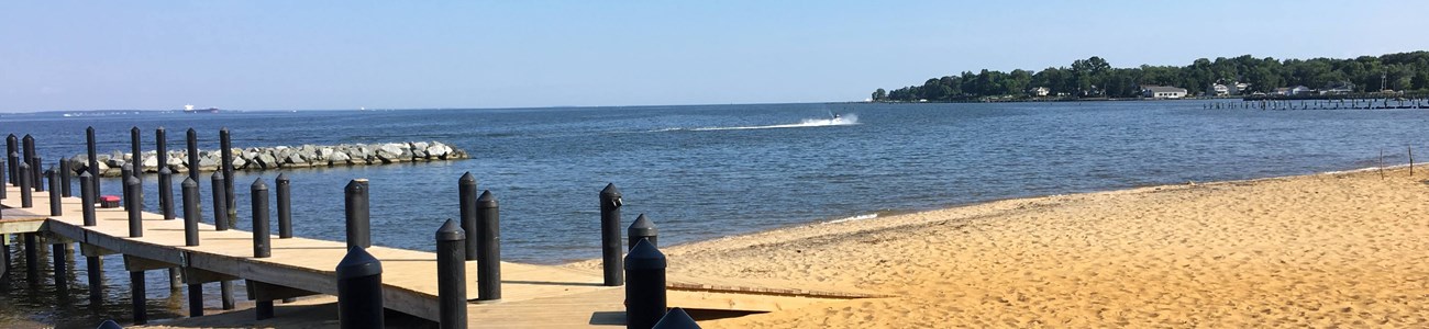 A dock extends from a sandy beach over water.
