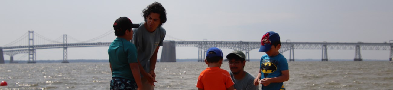 Three young boys speak with ranger interns on a sandy beach.