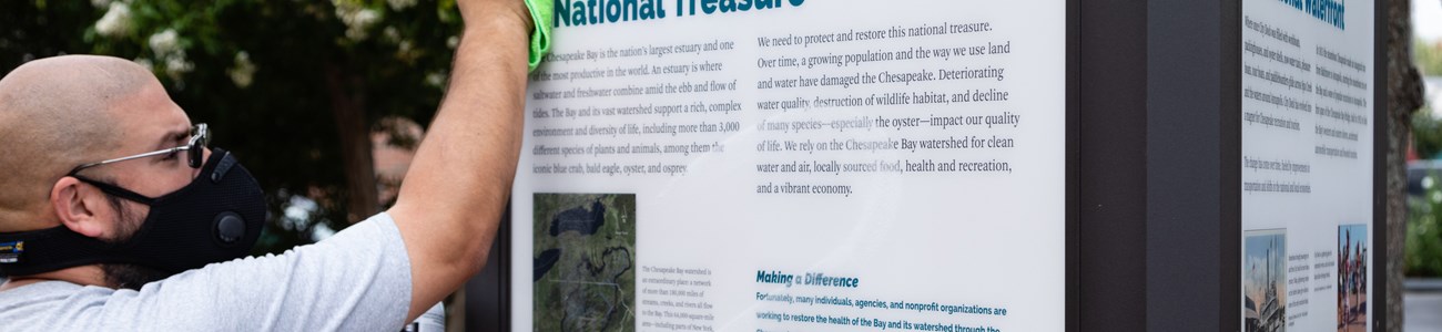 27 Work With Us Header A man wipes down an interpretive sign titled "National Treasure."