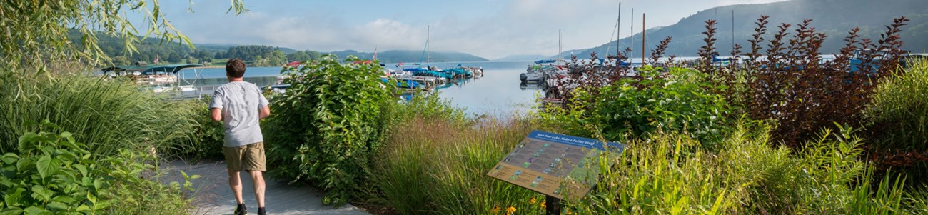 31 New York Gateways Header A man runs along an overlook trail high above a waterside town.