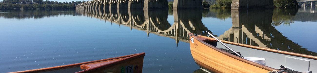 32 Pennsylvania Gateways Header Two canoes docked in the foreground with a bridge extending over water into the distance.