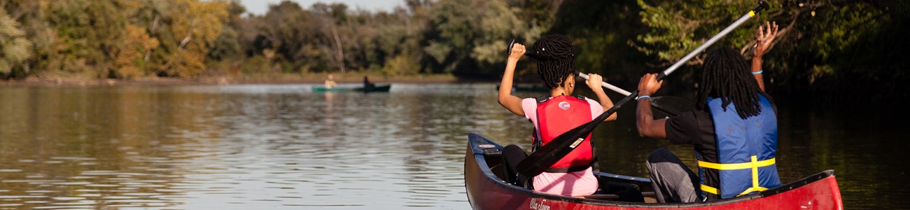 Two people paddle a red canoe through water.