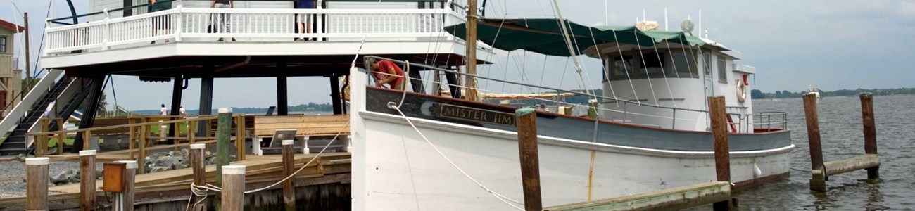 A skipjack docked beneath a restored and relocated screw pile lighthouse.