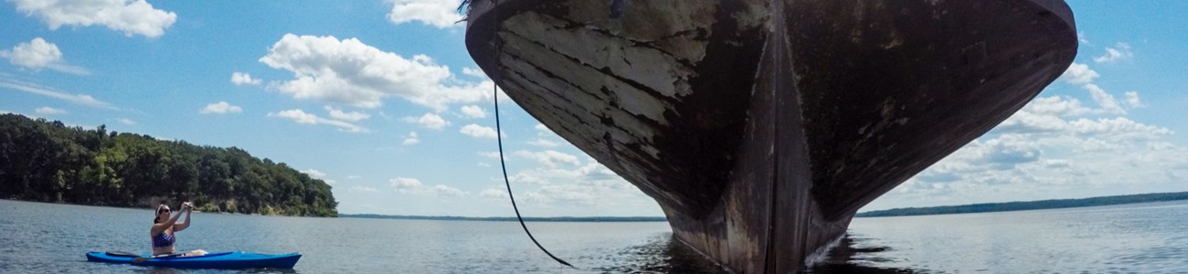 A woman in a kayak takes a picture of the grounded remains of a ship's hull.