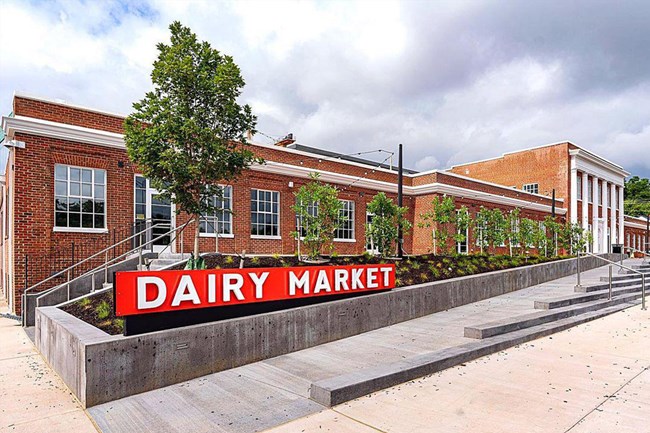 Brick building labeled "Dairy Market" with landscaped area and concrete walkway.