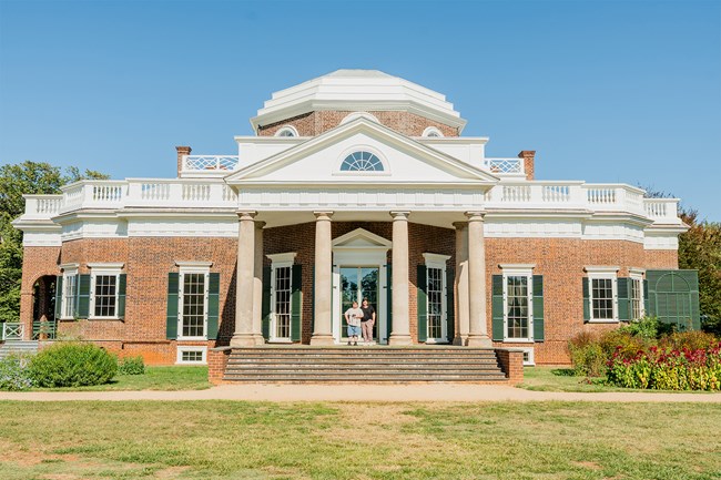 Historic brick building with columns and a dome, with people standing at the entrance.