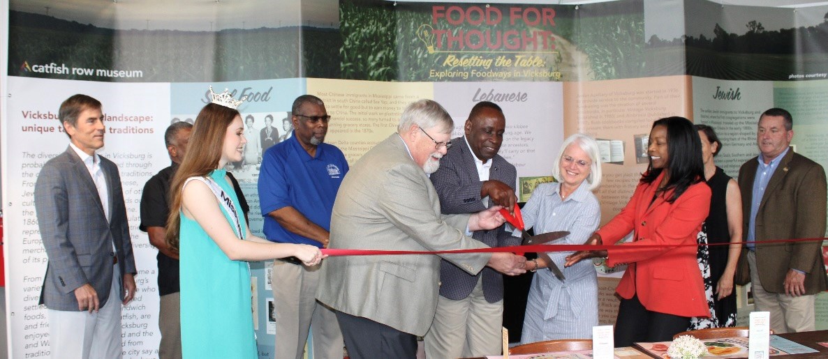 lt= A group of people cut a red ribbon to open the Resetting the Table Exhibit