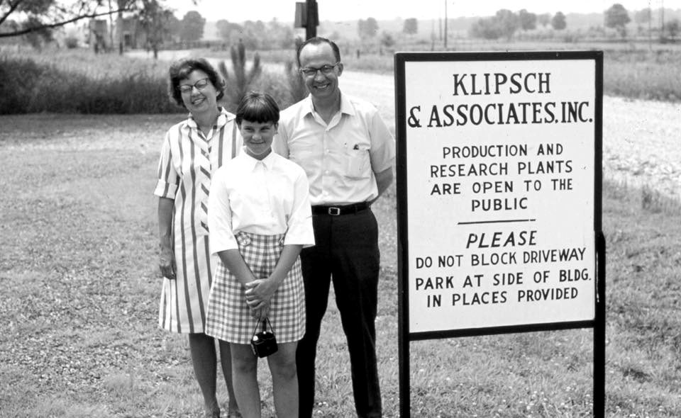 Three people are standing next to a sign for Klipsch & Associates, Inc.