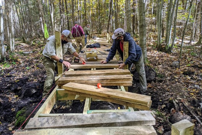 Ice Age Trail Alliance NPS People lay planks on a boardwalk within a forest.
