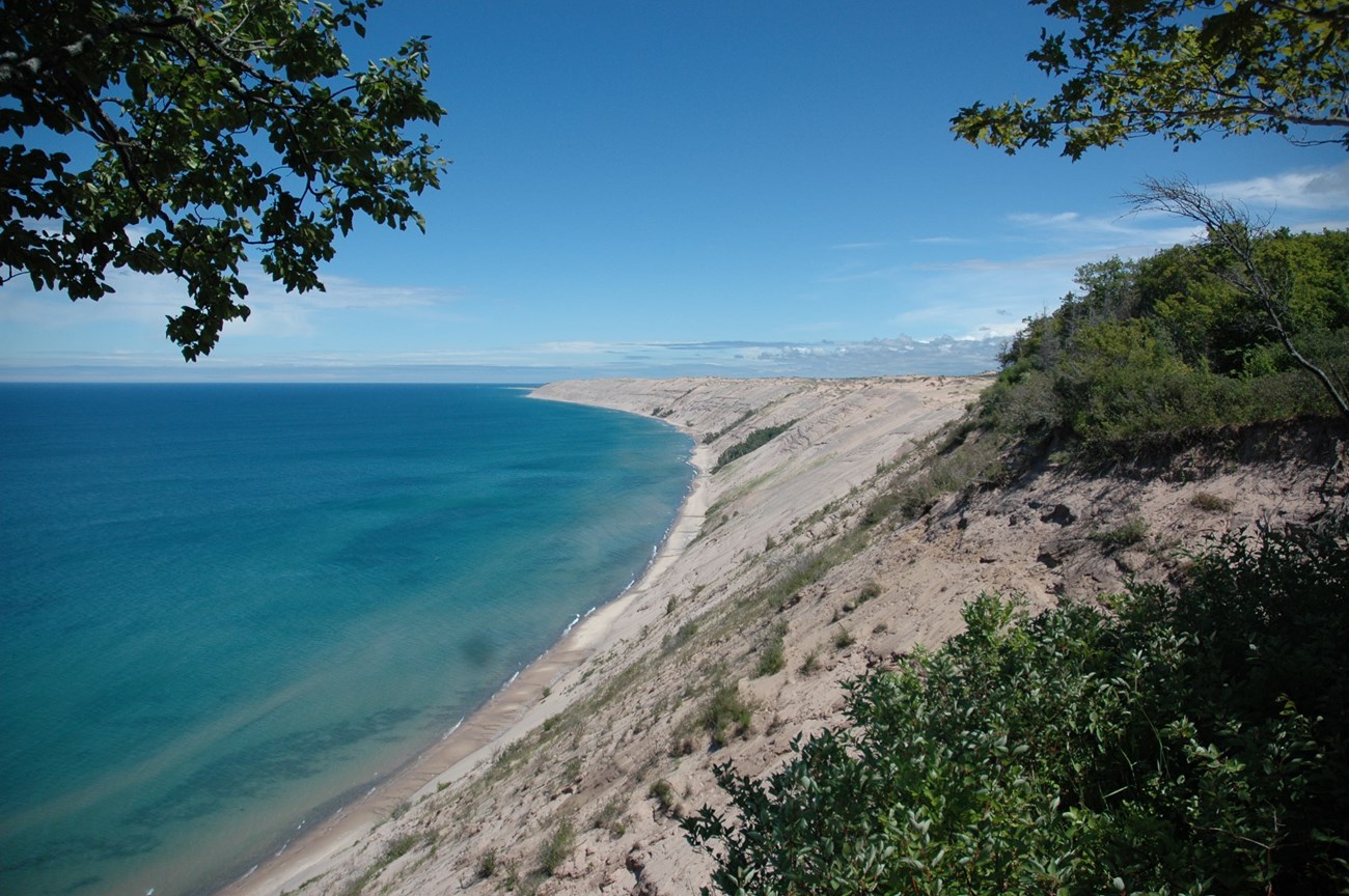 Dunes rise above shoreline under blue sky.