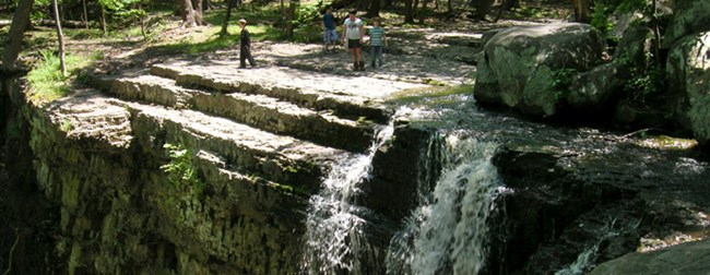 people standing next to a small waterfall on a rock ledge
