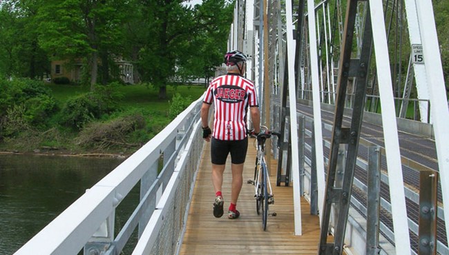 person walking a bike across a bridge