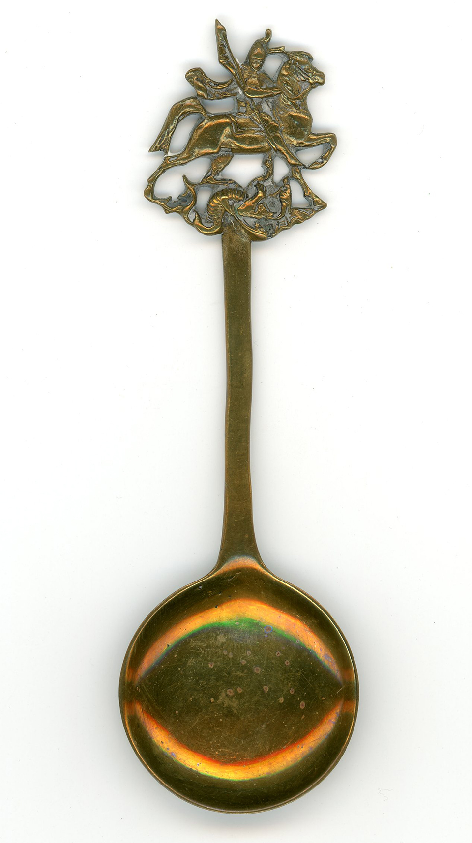 A brass spoon with circular bowl and an image of St. George slaying the dragon on the end of the handle. A brass spoon with circular bowl and an image of St. George slaying the dragon on the end of the handle.