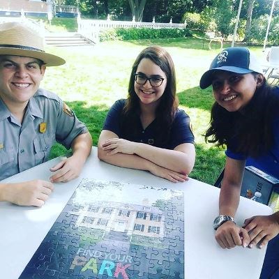 Find Your Park Volunteers A ranger and two volunteers with a Find Your Park puzzle on the Longfellow front lawn