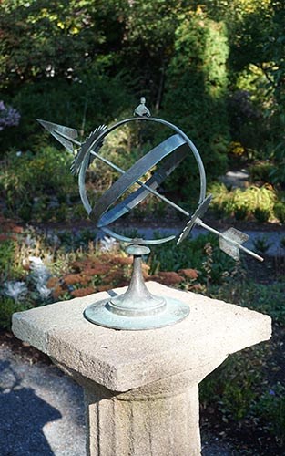 Sundial made of arrow intersecting two circles set at right angles standing on pedestal