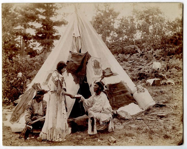 Native American man proposes on bended knee to Native American woman in front of wigwam