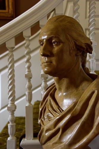 Bust of George Washington in front of stair railing.