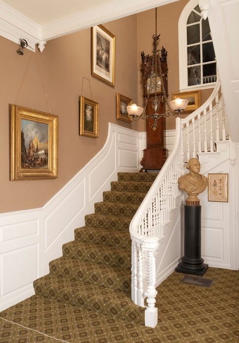 Hallway with stairs with a grandfather clock on the landing and bust of George Washington at the foot.