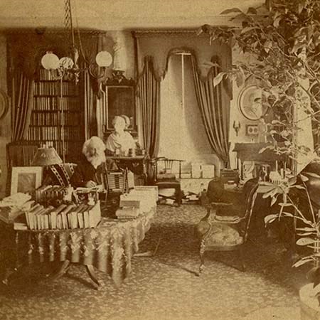 Black and white photograph of bearded man sitting at table covered in books