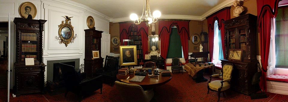 Panorama of interior of room filled with bookcases, desks, and red carpet and drapes