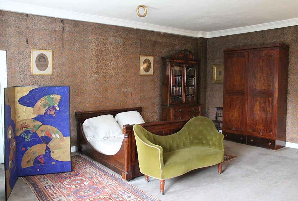 Interior of bedroom with sleigh bed, wardrobe, and sofa; gold ring attached to ceiling
