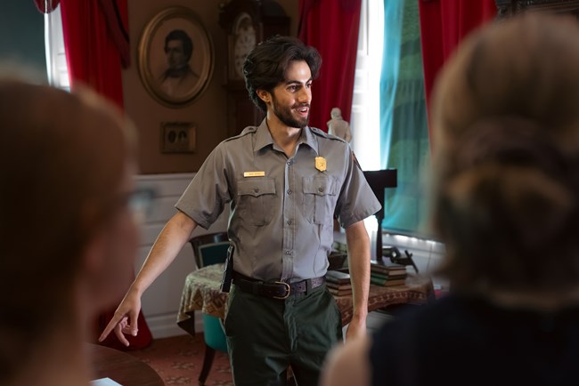 Park ranger stands in a historic study and points to an object on a table