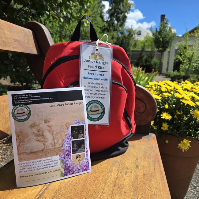 Landscape Junior Ranger book with red activity backpack on an outdoor bench next to yellow flowers.