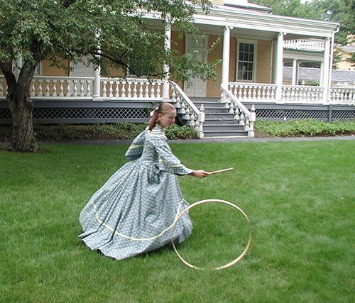 Hoop and Graces Girl in blue Victorian dress running with hoop and stick