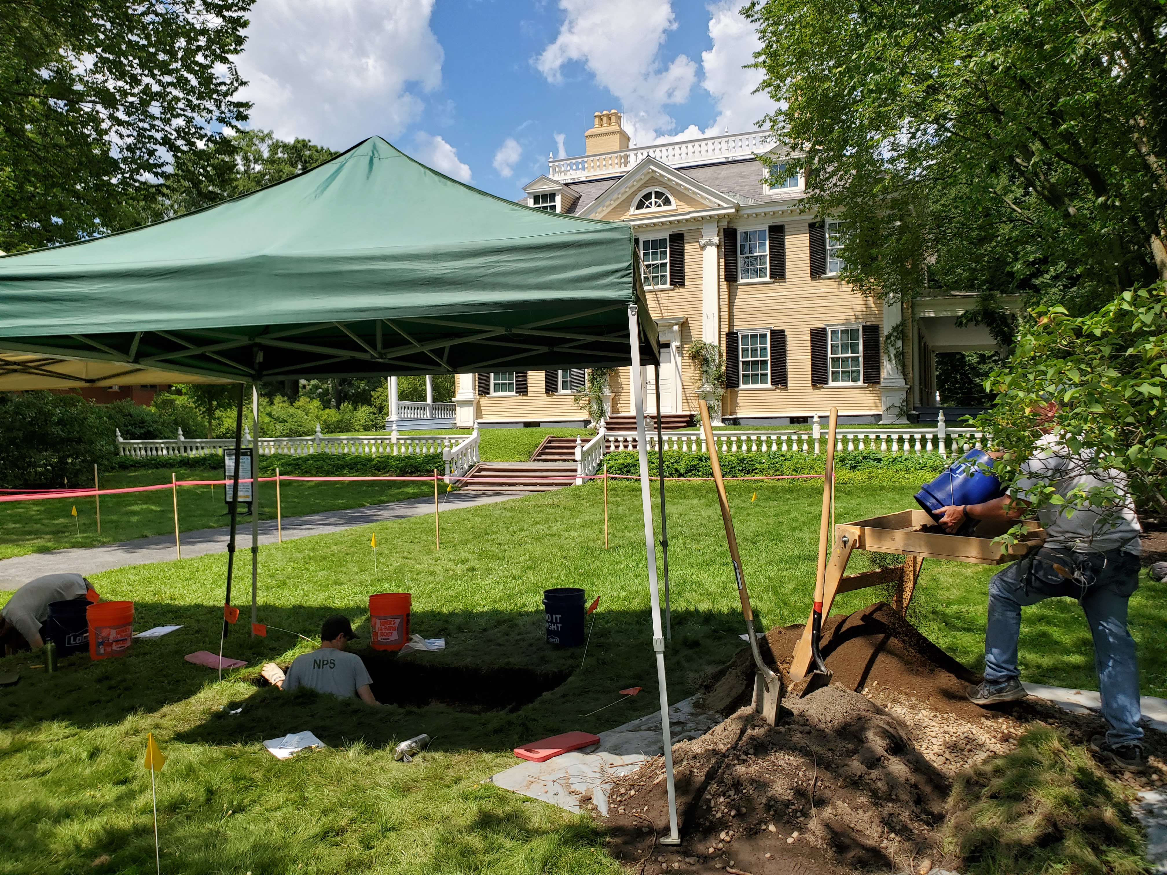 Archeologists working under a tent in front of historic house