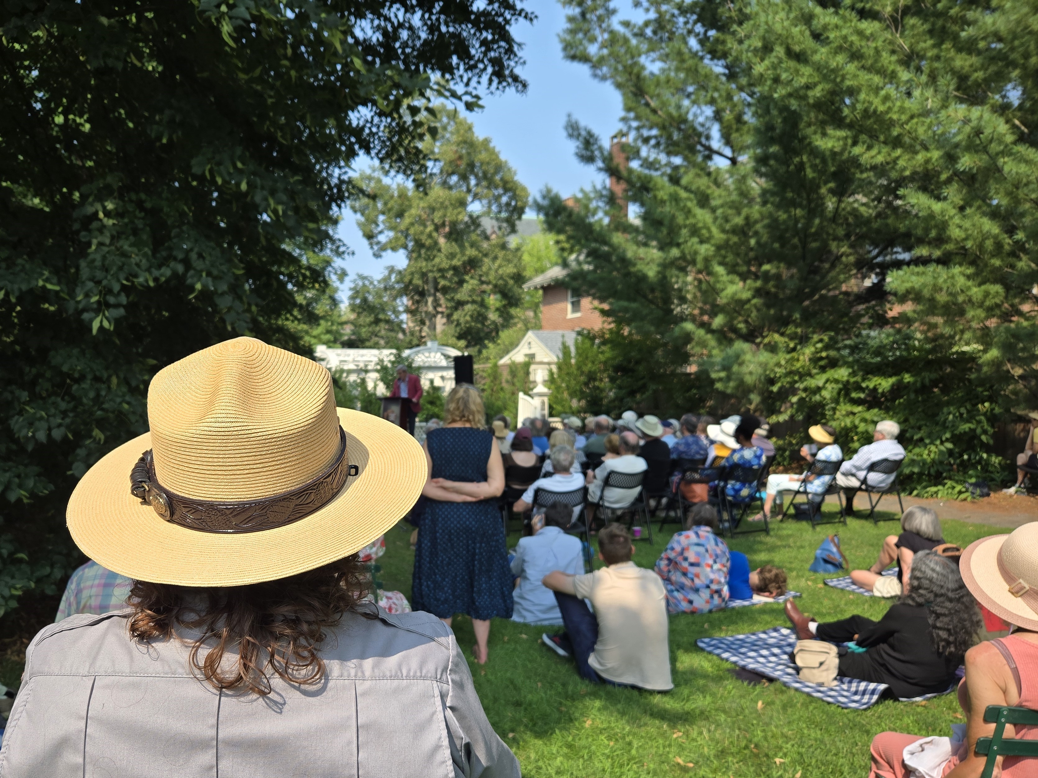 Crowd listens to an outdoor poetry reading, park ranger in foreground with back to camera