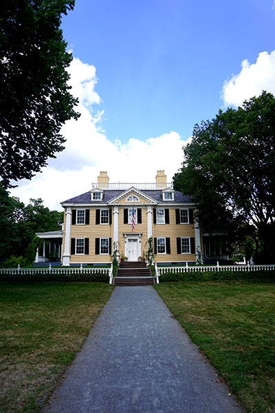 Image of large yellow house with white trim and dark green shutters. The picture is framed vertically, allowing a background of deep blue sky interspersed with fluffy white clouds. Image of large yellow house with white trim and dark green shutters. The picture is framed vertically, allowing a background of deep blue sky interspersed with fluffy white clouds.