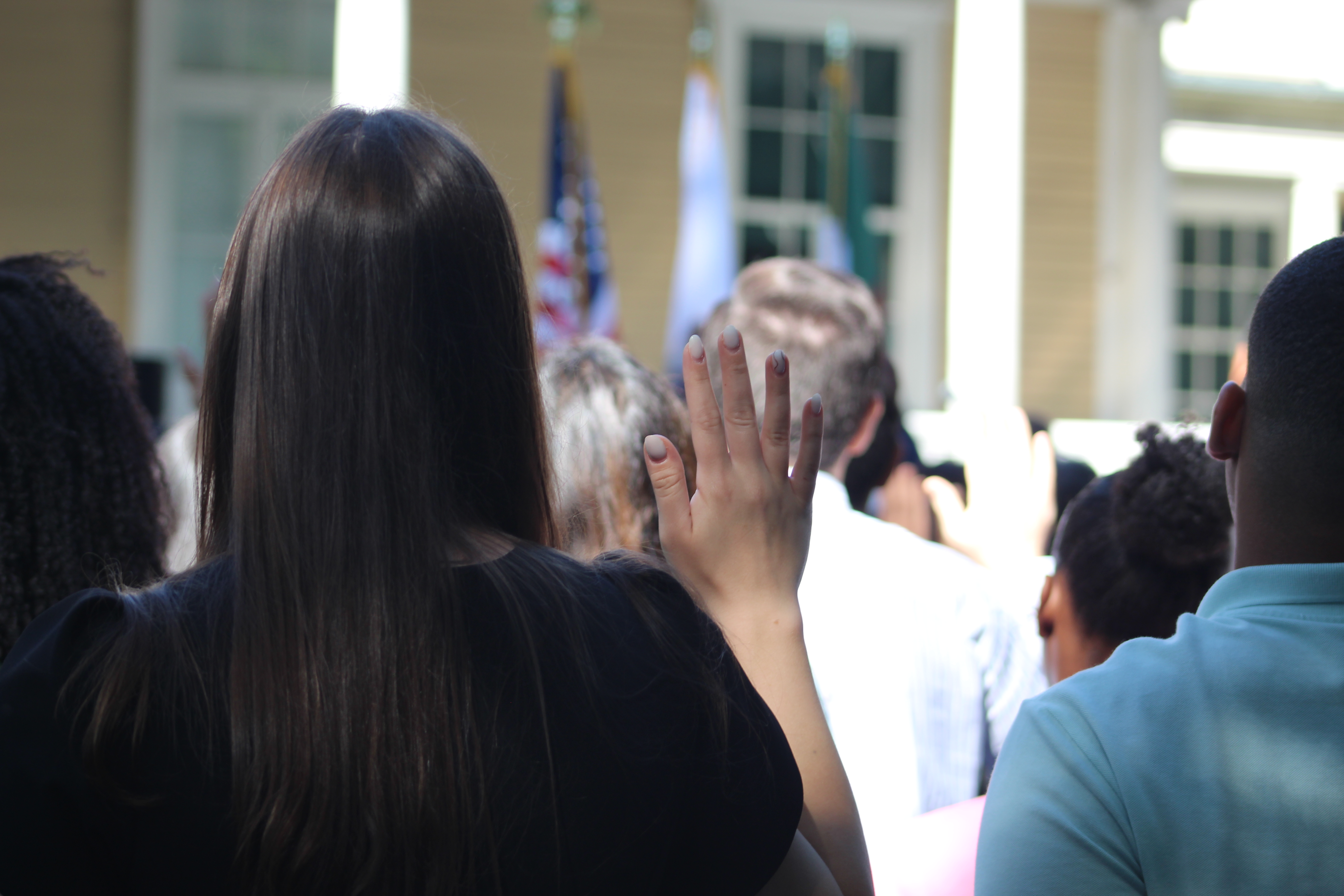 Naturalization ceremony at Longfellow House-Washington's Headquarters New citizens face away from the camera while raising their right hands.