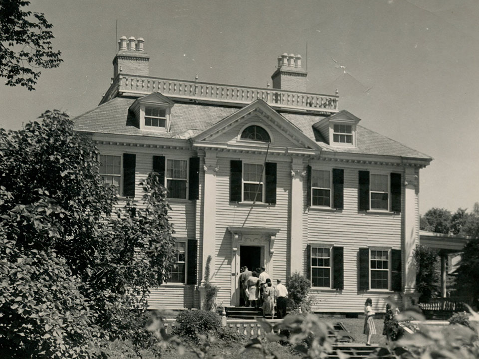 Black and white photo of visitors entering Longfellow House through front door