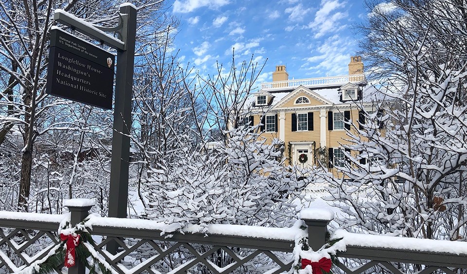 Georgian mansion with snowy trees and bows on fence in foreground