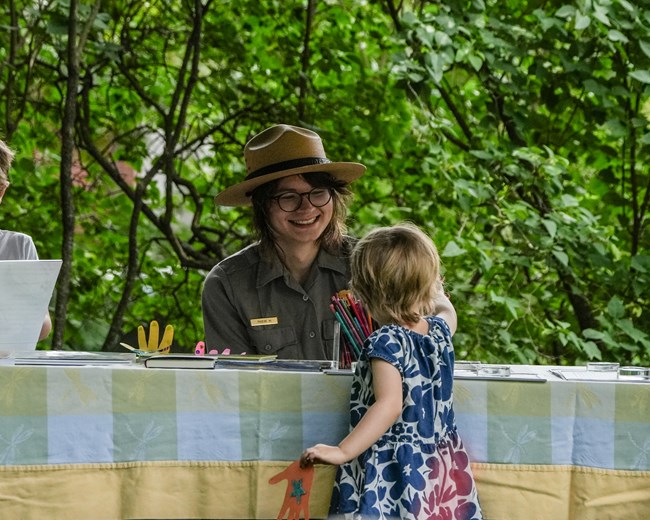 Park ranger at an activity table facing a young child