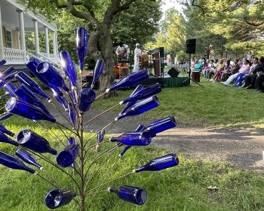 Blue glass bottle artwork with performers and audience behind