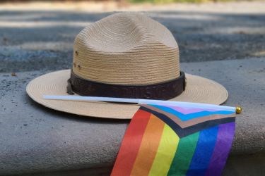 National Park Ranger flat hat on outdoor steps with rainbow progress pride flag