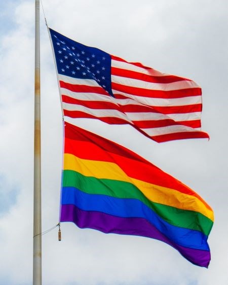 An American flag flying above a Pride flag, on the same flagpole