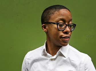 Portrait of Donika Kelly wearing a white shirt and glasses on a green background