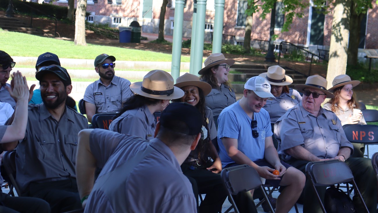 A group of park employees wearing a variety of uniforms smile and sit together