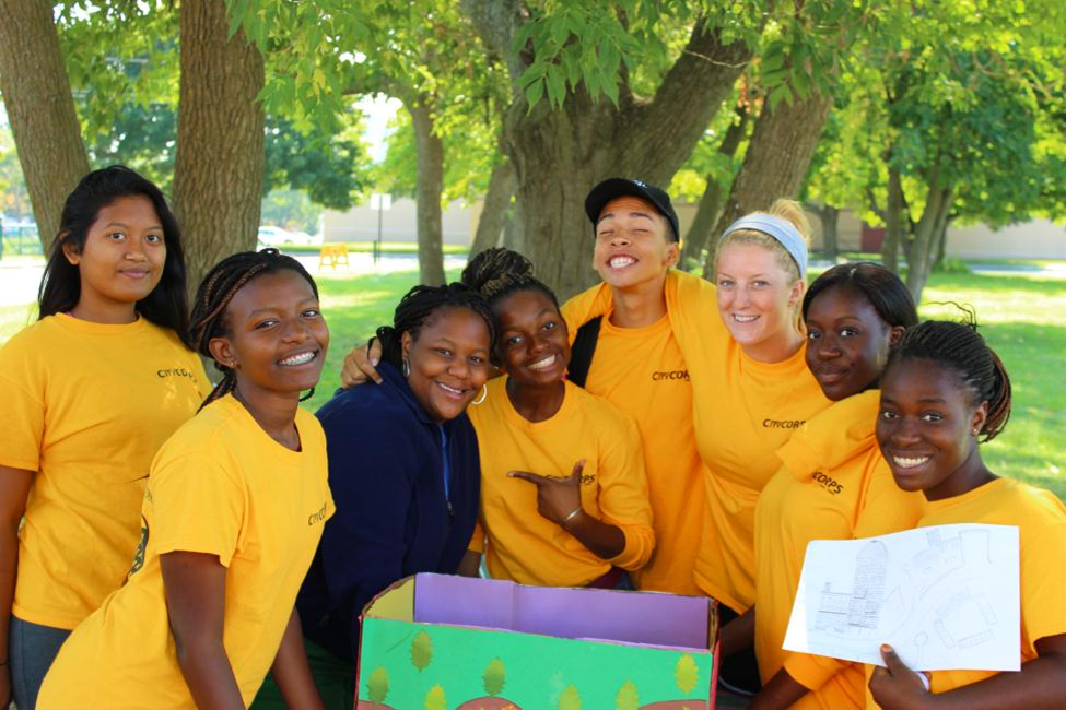 A groups of youths working on a time capsule outside under a tree.