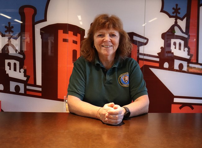A woman wearing a green polo smiles at an information desk.