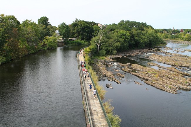 Walkway atop the Great River Wall along a canal with visitors walking.