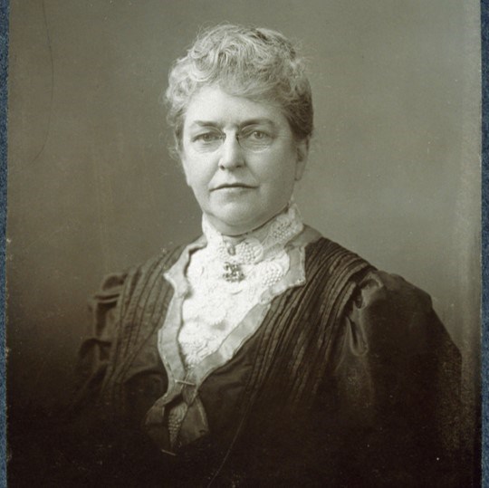 Helen Augusta Whittier A grayscale portrait of an older woman dressed in late 19th century dress looking straight out.