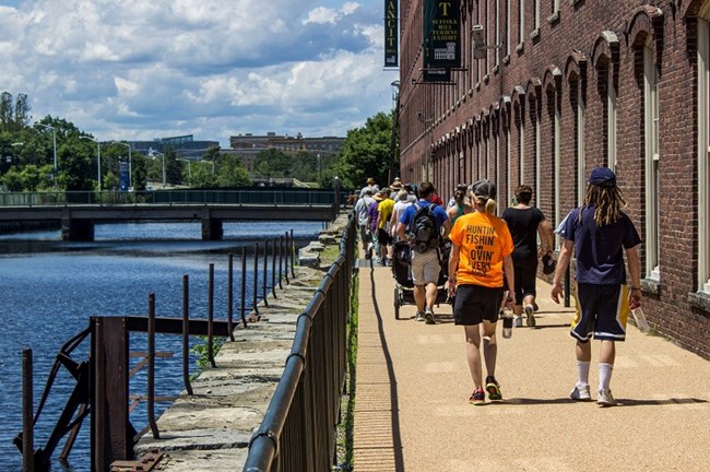 A group of visitors hiking along the Northern Canal and Suffolk Mill during an Urban Hike.