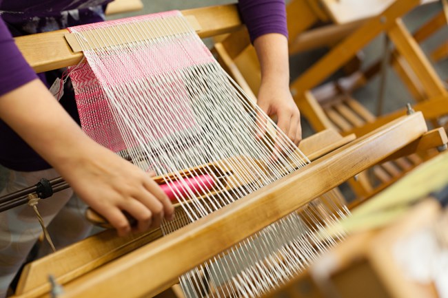 Close up of a kids hand's weaving fabric on a loom